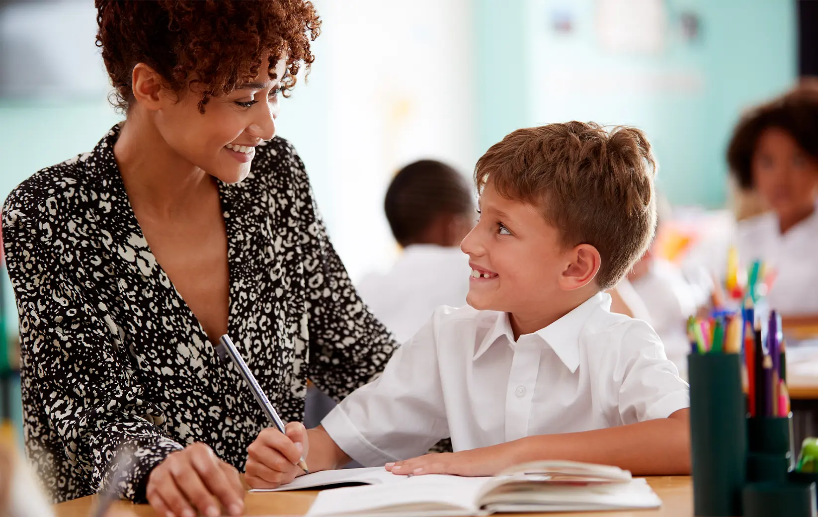 Tutor assists a young student with schoolwork in a classroom setting.