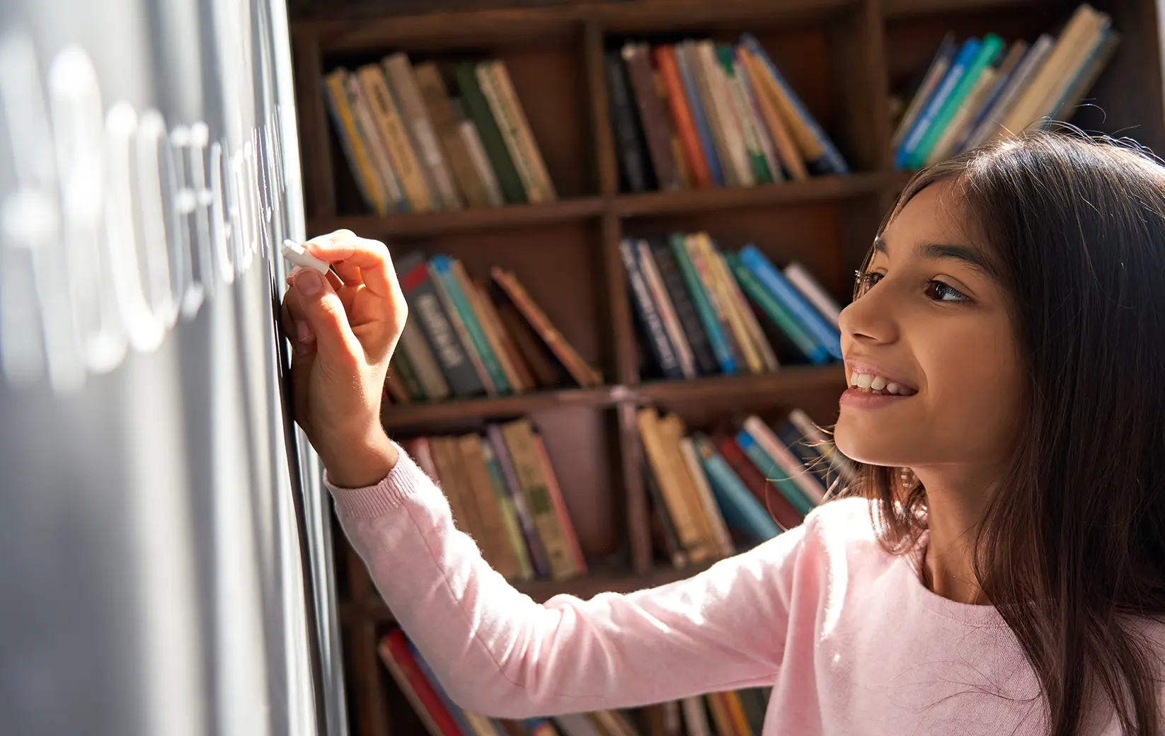 Child writing on a blackboard with bookshelves in the background