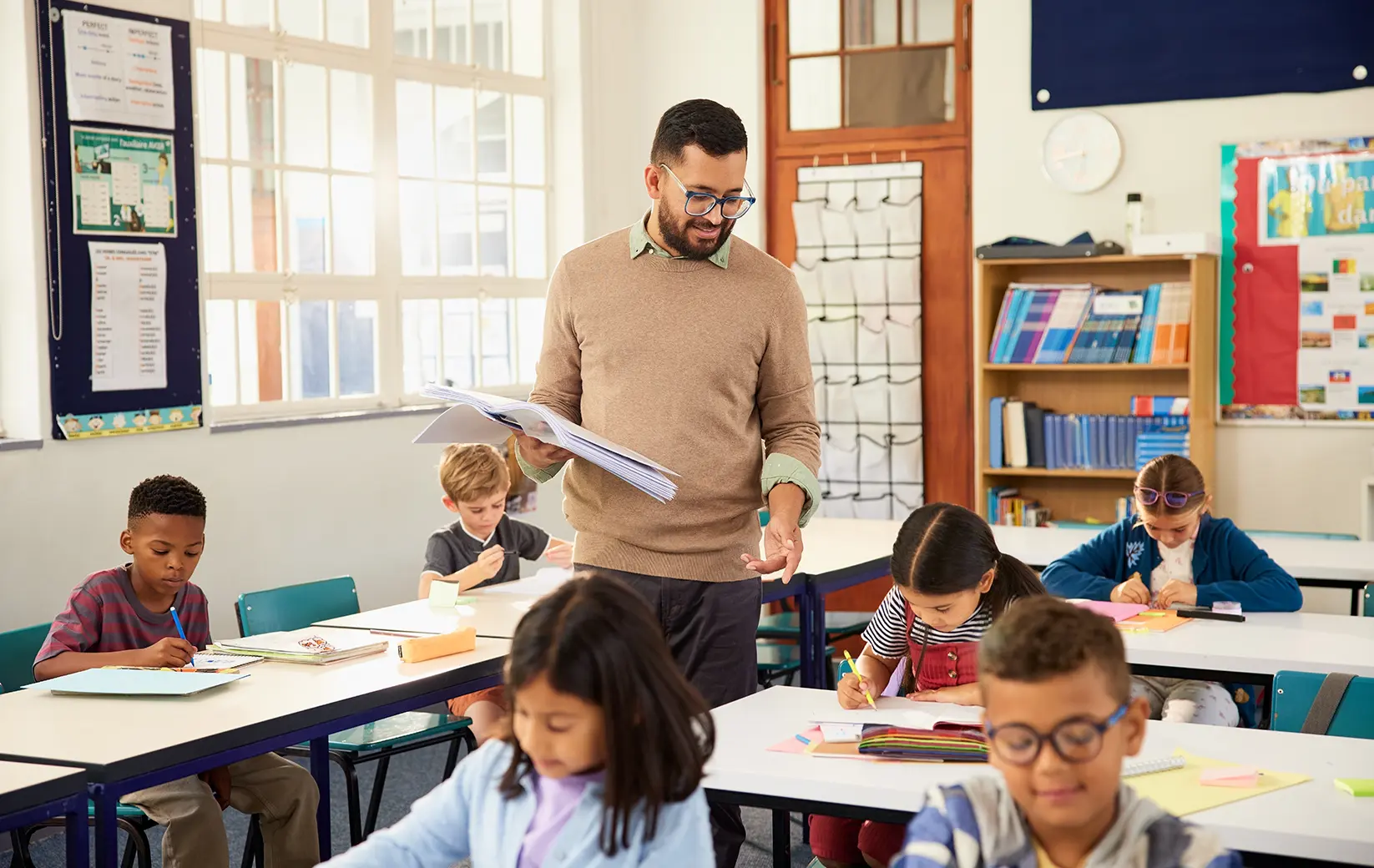 A teacher supports students working on assignments in a bright classroom.