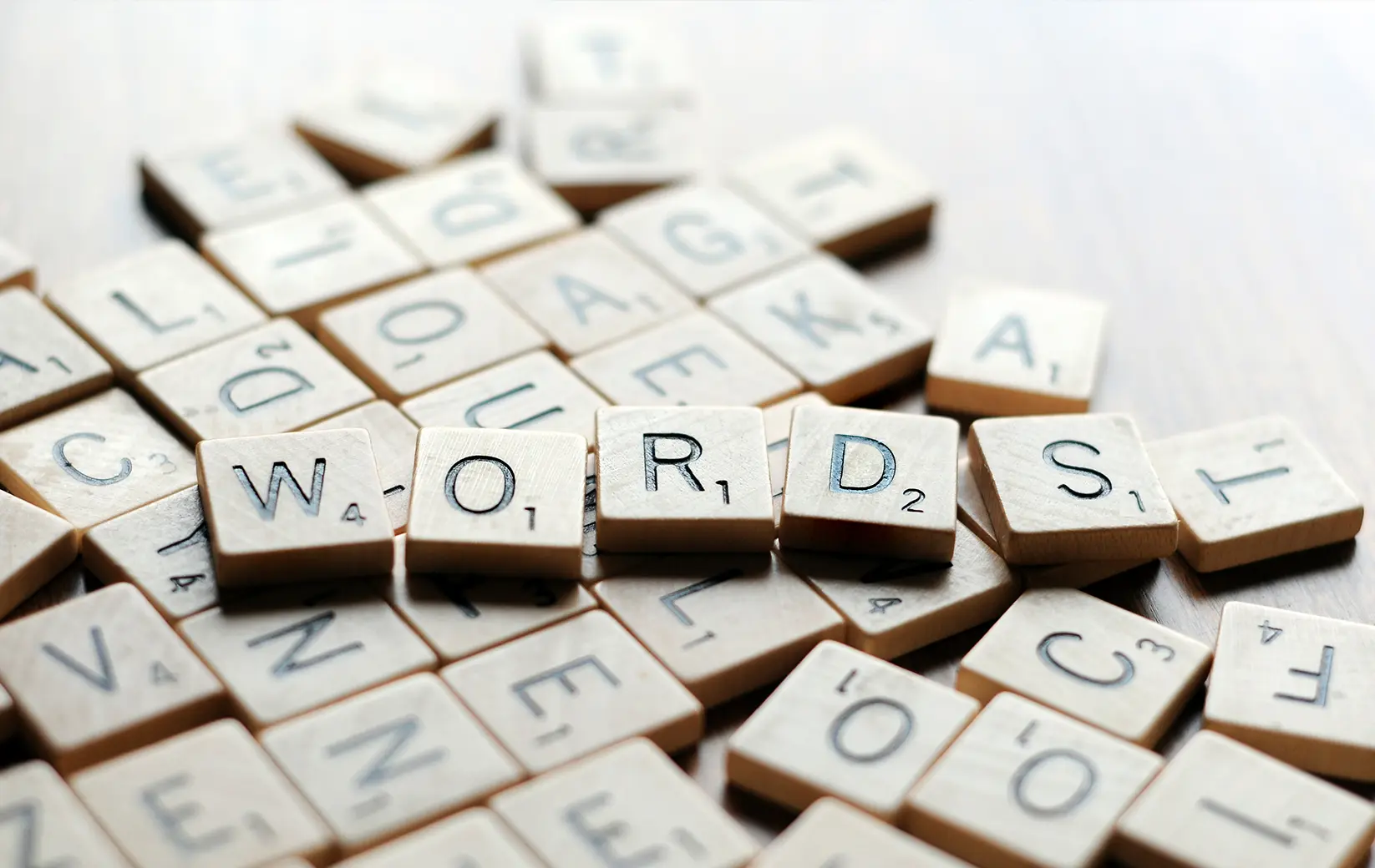 Scrabble tiles spelling "WORDS" on a wooden surface.