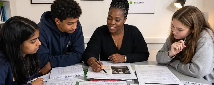 Tutor guiding students through study materials at a desk