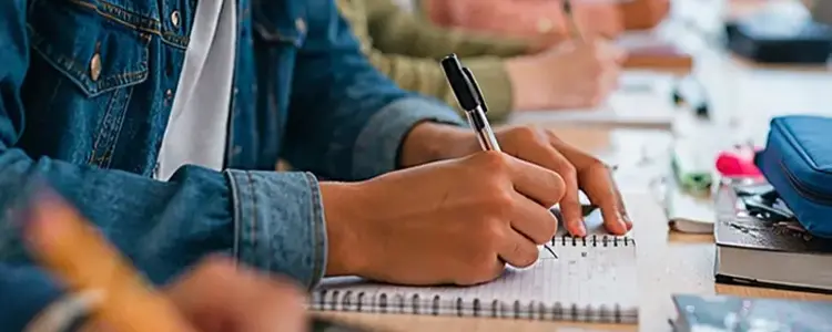 Student taking notes with a pen in a classroom setting